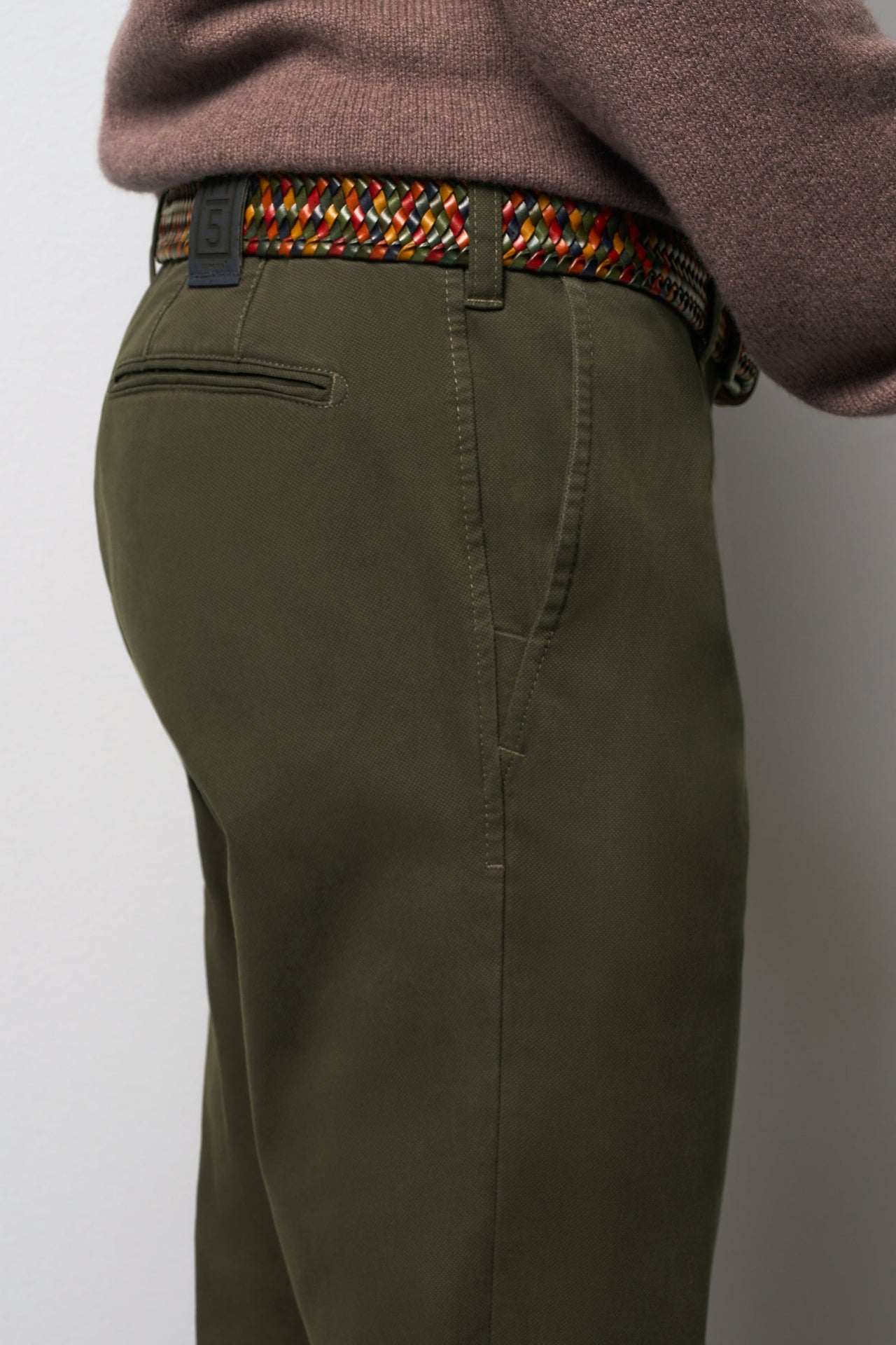 Person wearing olive green pants with a colorful belt on a plain background